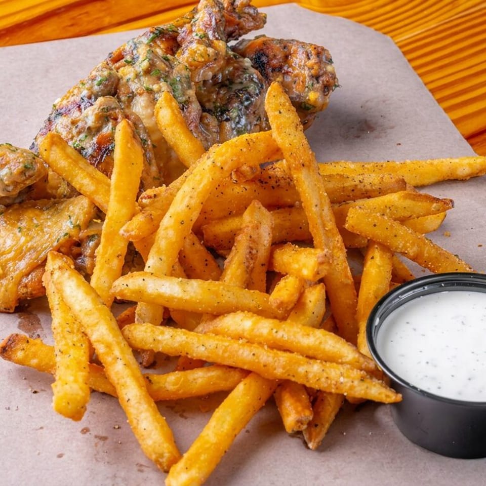 Crispy fried chicken wings and seasoned fries served with creamy dipping sauce on parchment over a wooden table.