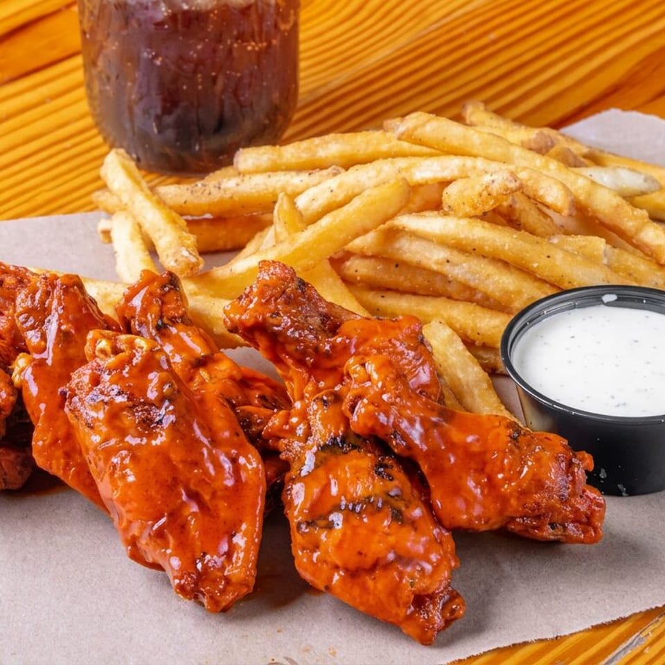 Buffalo chicken wings with French fries and creamy dipping sauce served on parchment over a wooden table.